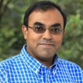 Amit Roy Chowdhury in blue plaid collared shirt and dark glasses in front of plant background
