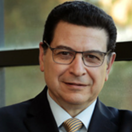 man wearing suit and tie in front of window with short black hair and glasses
