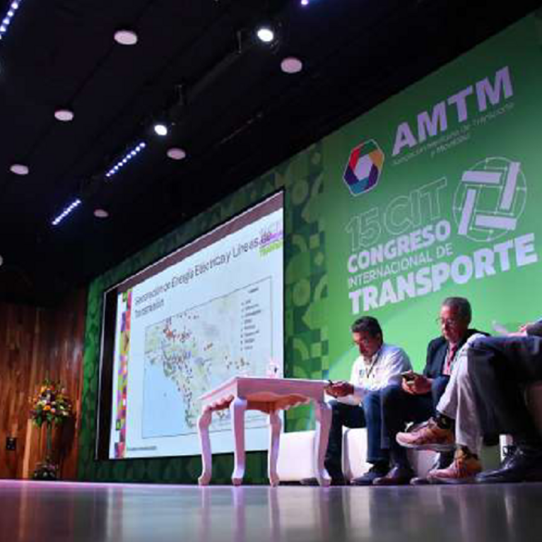 A speaker presents at the 15th International Transport Congress in Mexico City, with four panelists seated on stage next to a large screen displaying a map. The AMTM logo and event name are visible in the background.