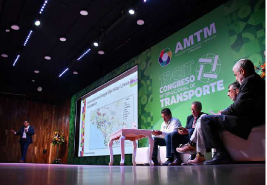 A speaker presents at the 15th International Transport Congress in Mexico City, with four panelists seated on stage next to a large screen displaying a map. The AMTM logo and event name are visible in the background.