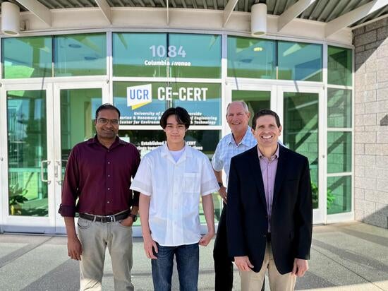 Warren Norbeck stands outside CE-CERT’s main entrance, positioned between mentors Zissimos Tsoutsanis on his left and Tom Durbin on his right. All three are posing in front of a large sign reading 'Light Duty Laboratory in Partnership with AVL,' with the UCR CE-CERT building address visible in the background.