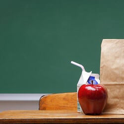 Brown bag lunch on a school desk in front of green chalkboard