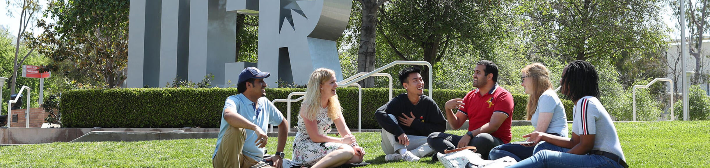 students sitting on the lawn in front of the UCR sign (c) UCR/Stan Lim