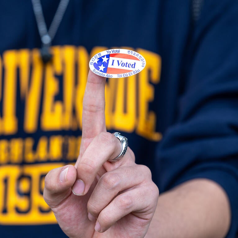 a person wearing a ucr shirt with an I voted sticker on their finger.