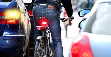 A bicyclist rides in between cars on their way to campus. 