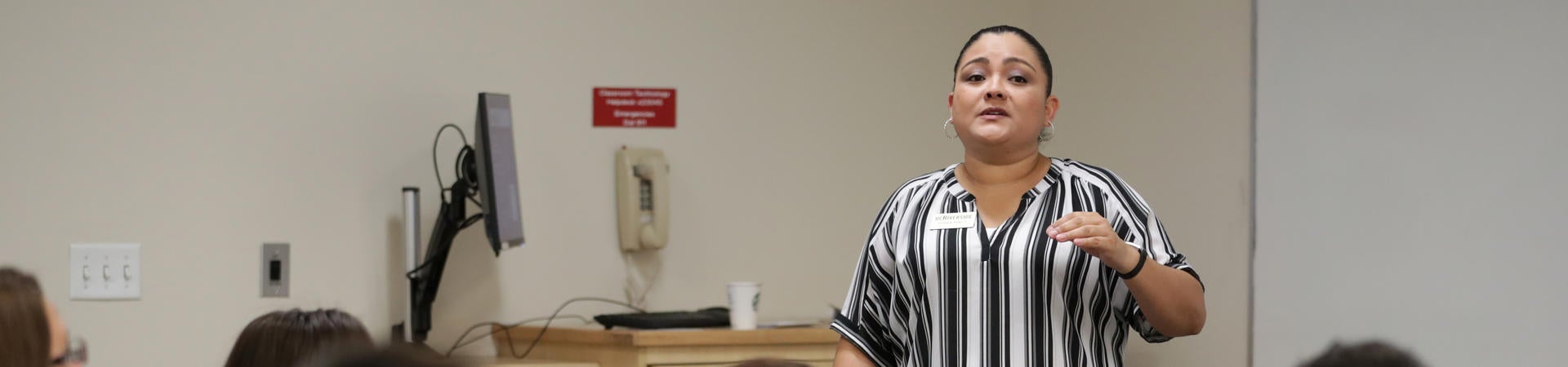 A presenter at TA Orientation stands speaking in front of seated graduate students