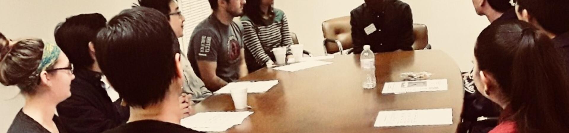 A group of TAs sit around a table piled with papers and coffee mugs