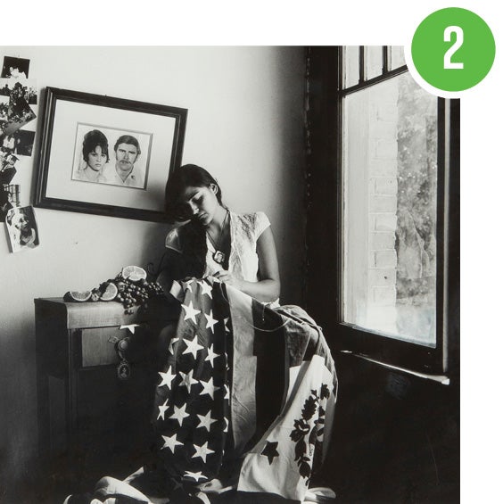 Black and white photograph of woman sewing an American and Mexican flag together