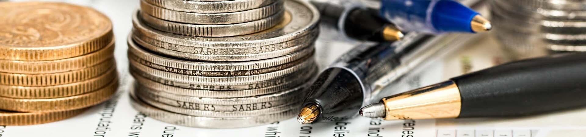 Stacks of coins and pens messily scattered over a spreadsheet