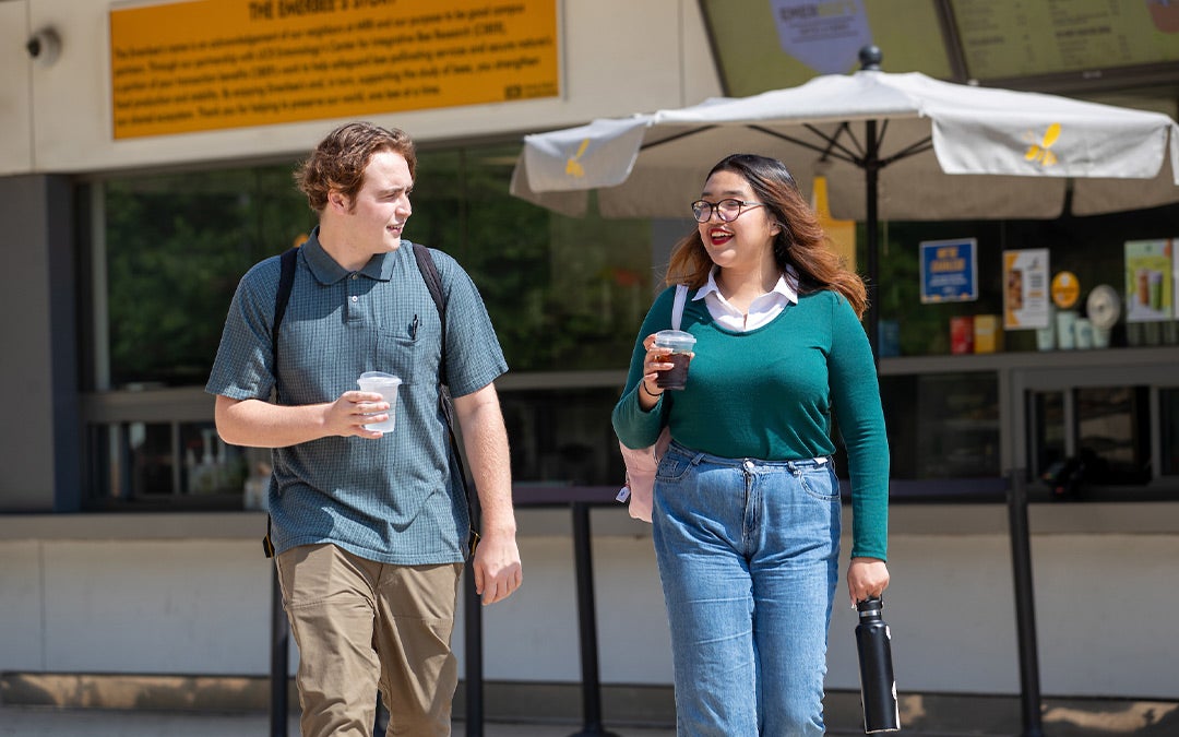 Dos estudiantes de UC Riverside caminando por el campus con bebidas en las manos