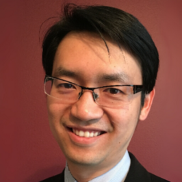 Man with black hair and glasses smiling in front of reddish brown background