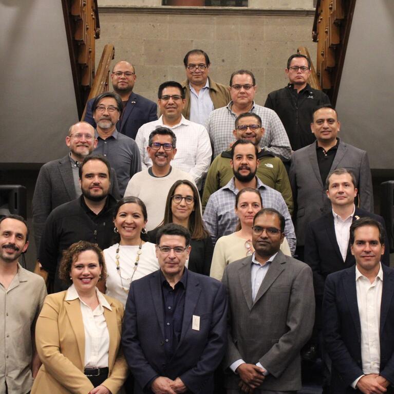 Twenty-two participants from the Binational Working Group on Zero-Emission Vehicles pose on a staircase at the Casa de la Universidad de California in Mexico City.