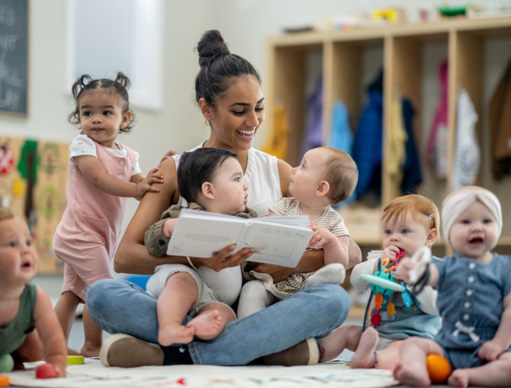 Young hispanic early childhood teacher on the floor reading with babies