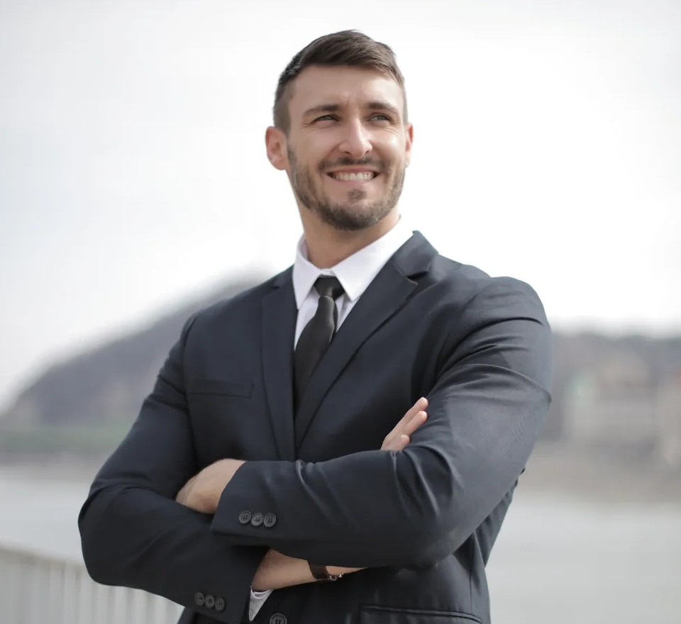 View from the waste up of a young White man in a business suit with arms crossed and smiling