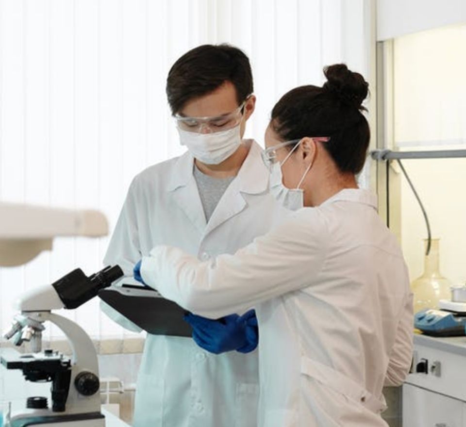 Two bioengineering professionals looking at some information in front of a microscope