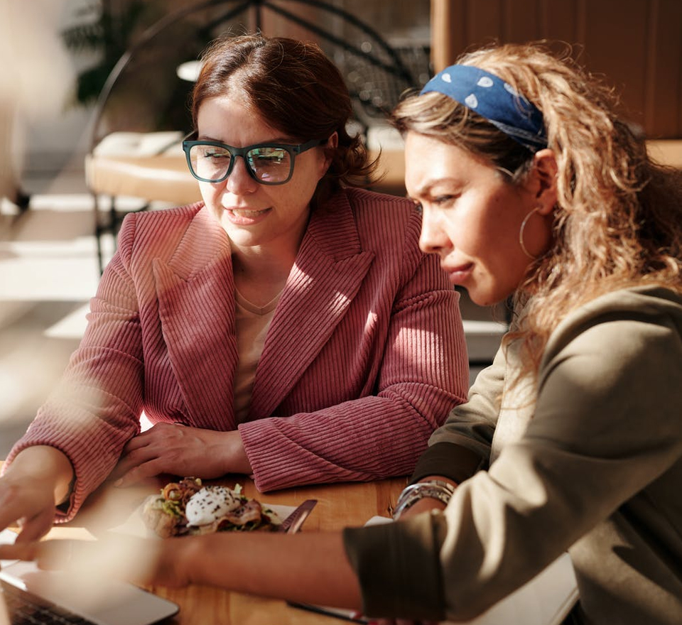 Two middle age women one White one Hispanic sitting outside at a table going over paperwork