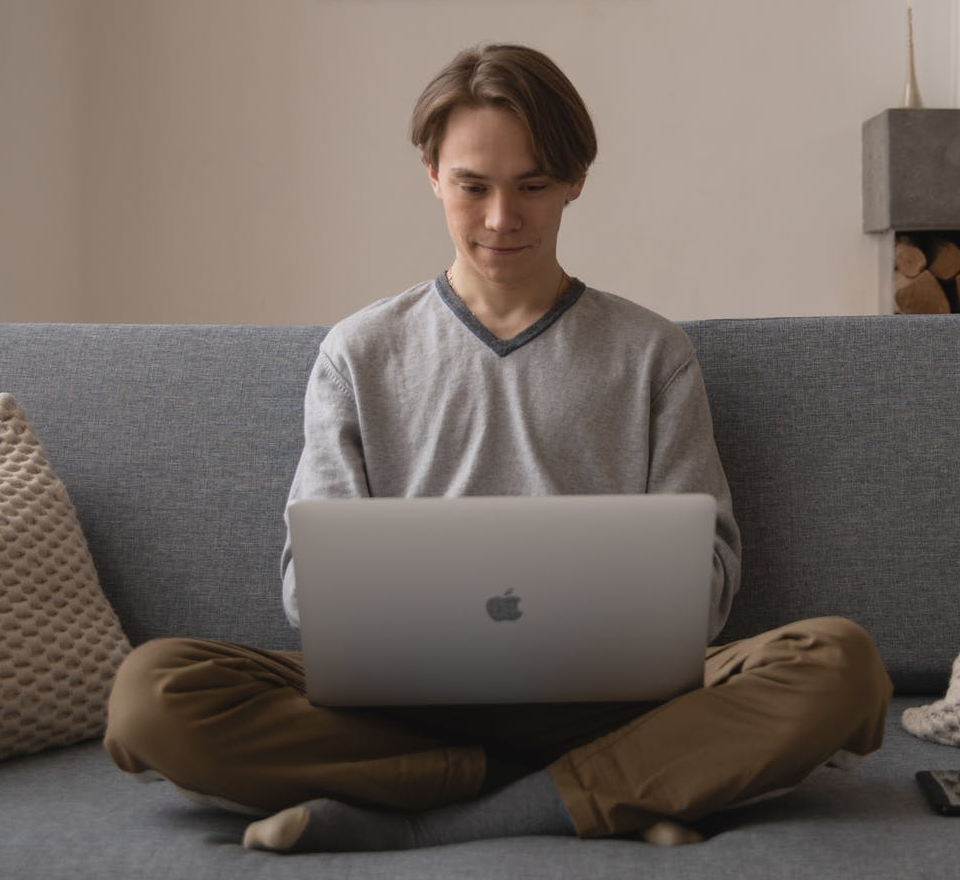 Young White man sitting cross-legged working on a laptop on a couch