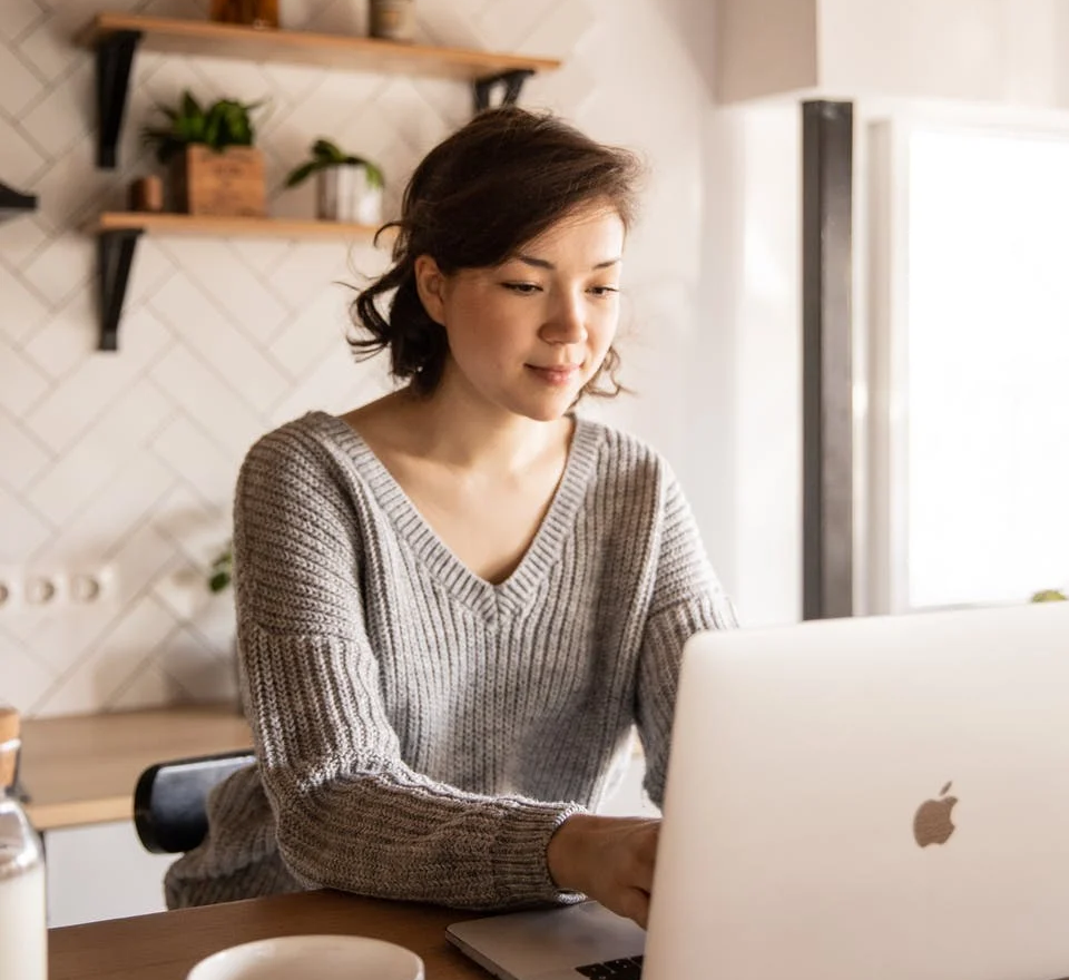 Young Asian woman sitting at kitchen counter working on a laptop