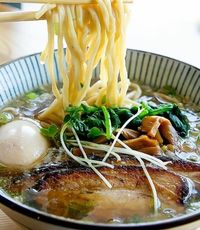 Bowl of ramen with spoon holding noodles over the hot broth with vegetables meat and an egg