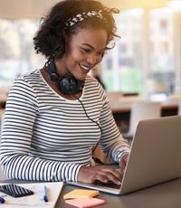 Young black female wearing headphones and sitting at a desk working on a laptop