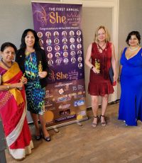 Noura Bishay and three other women standing next to a poster holding an award