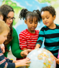 Multicultural kindergarten kids looking at a globe with their teacher