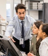 Male High School teacher working with two female students in a computer lab