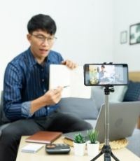 Male Asian teacher showing assignment in front of camera to online students