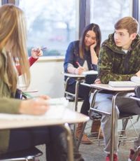 Students in a high school classroom sitting in desks and talking to one another across the aisles