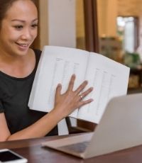 Teacher holding a textbook in front of the laptop to show online students