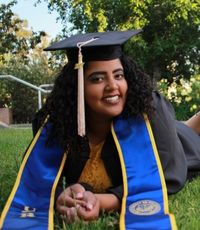 UCR University Extension graduate Sahara Powell lying in front of the UCR letters in her grad regalia