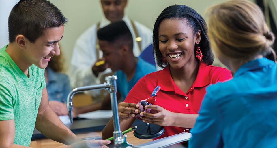Diverse group of 3 highschool student smiling and looking down at the same think in the classroom