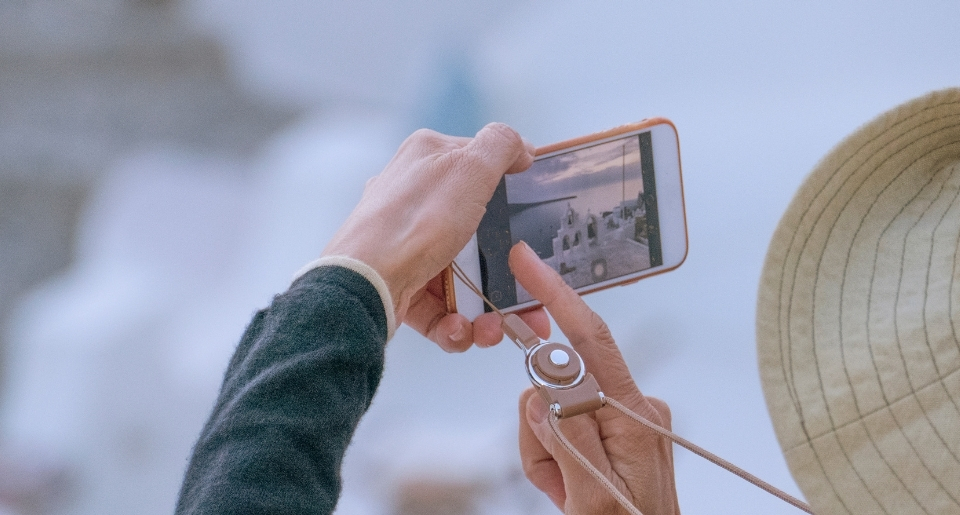 Womans hands holding a mobil phone focusing on an image of a while architecture near a large body of water