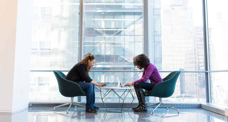 Two women sitting across from one another at a table working on laptops