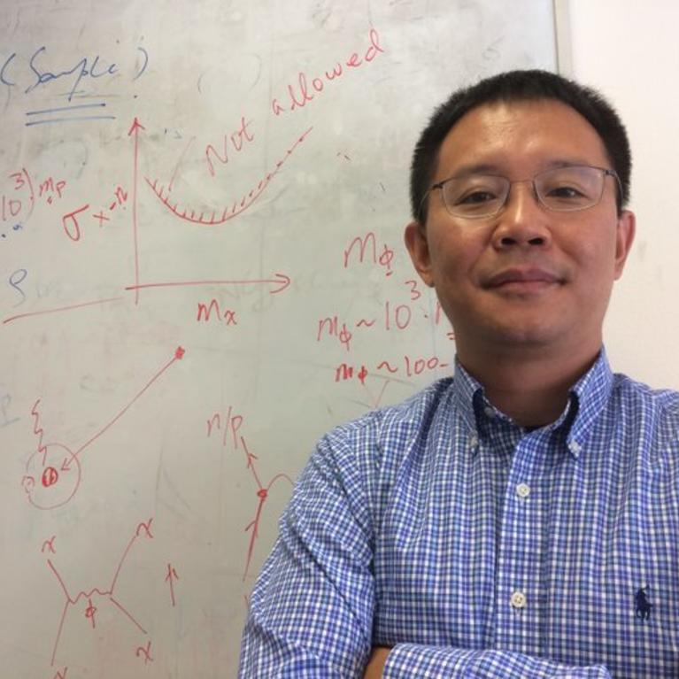 Professor Hai-Bo Yu poses in front of a whiteboard full of physical diagrams and equations.